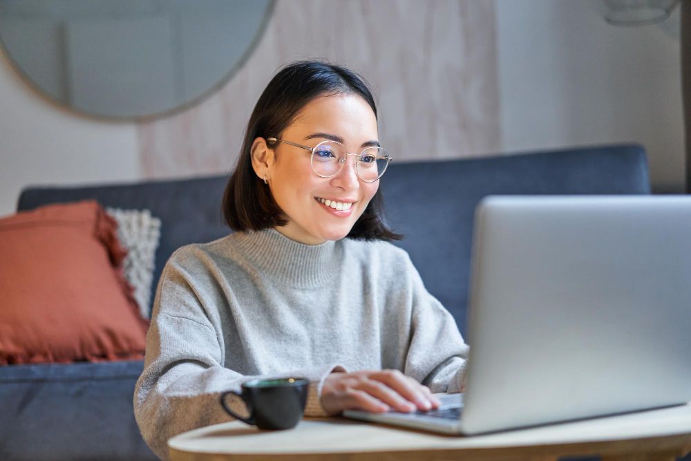 Chica trabajando en su portátil, muy sonriente y relajado junto a una taza