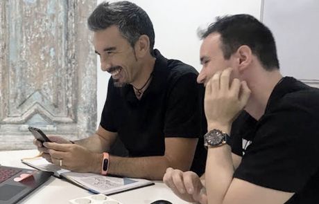 Dos profesores de Artes Creativas sentados a una mesa con cuadernos, muy sonrientes y vestidos con camisetas negras