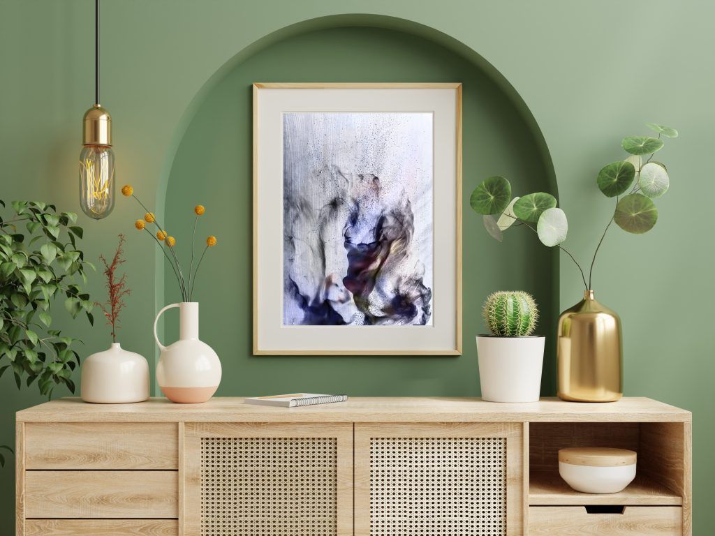 Espacio interior en color verde, vemos un mueble de madera clara, elementos decorativos en color dorado, cerámica blanca y plantas y un cuadro abstracto en el centro de la composición