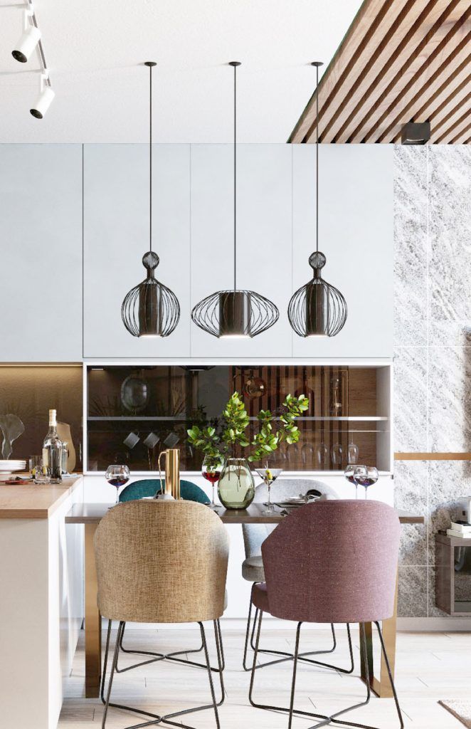 Fotografía de una cocina donde vemos la zona de comer, es muy agradable, la mesa es baja de madera, está puesta con jarrones y copas bonitas de vino, como si estuvieran a punto de comer, las sillas parecen cómodas y son de colores pastel, encima cuelgan tres lámparas.