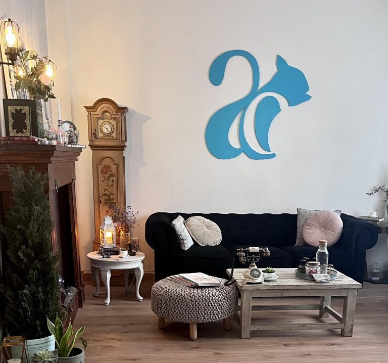 Espacio de Artes Creativas, en concreto la zona de estar del estudio donde encontramos un espacio acogedor con sofá, chimenea y elementos decorativos muy agradables que invitan a estar en el lugar, la pared del fondo tiene el logotipo en grande