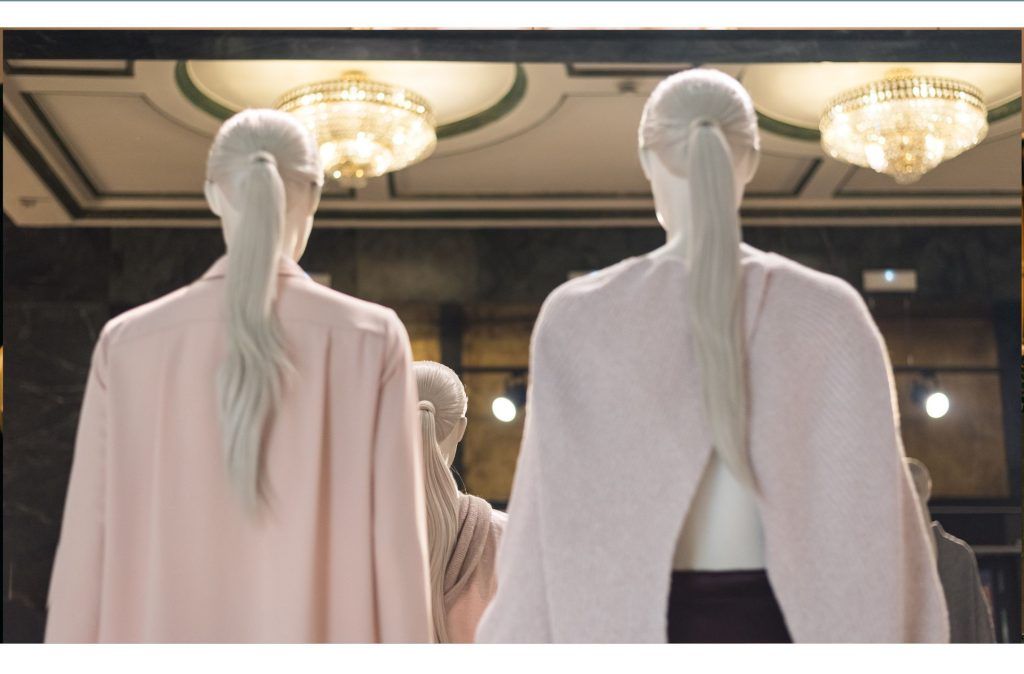 En la imagen vemos varios maniquies femeninos de espaldas, el espacio donde se encuentran es elegante de techos altos con molduras y lámparas colgantes de crsital